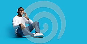 Happy handsome young african guy listening to music on blue