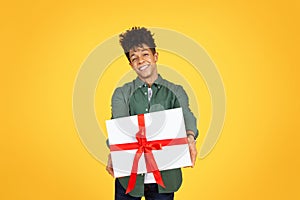 Happy handsome young black guy giving present, yellow background photo