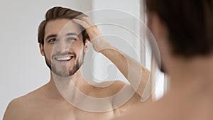 Happy handsome young guy combing smooth brown hair with fingers
