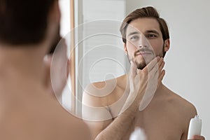 Happy handsome young man applying lotion or balm on stubble