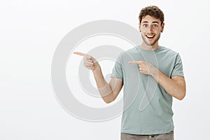 Happy handsome young man with earrings, pointing left with index fingers and smiling joyfully, showing something awesome