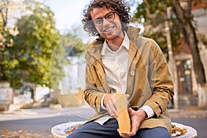 Happy handsome young man reading and posing with book outdoors. College male student carrying books in campus in autumn street.