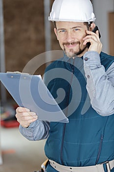 happy handyman holding clipboard in hand and making call