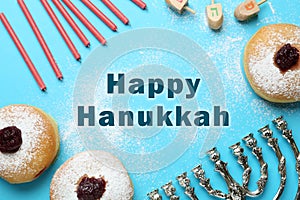 Happy Hanukkah. Traditional menorah, candles, sufganiyot and dreidels on light blue background, flat lay