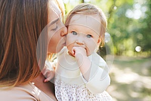 Happy harmonious family outdoors. mother kissing her baby, playing in the summer on the nature