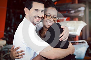 Happy Harmony people at workplace, smiling white man and African American worker hugging each other showing love and respect in