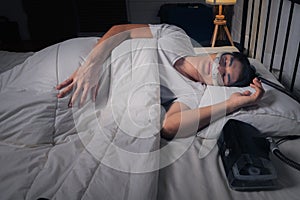 Happy and healthy Asian man with CPAP machine on side table wearing CPAP mask sleeping smoothly in bed all night without snoring
