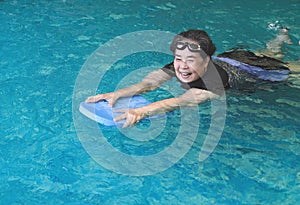 Happy and healthy Asian senior woman swimming with kickboard in a swimming pool. Smiling old woman swimming with inflatable board