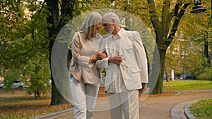 Happy healthy elderly senior mature Caucasian grandparents married man woman family couple walking holding hands outside