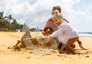 Happy healthy family father and daughter building sand castle on beach smiling and carefree