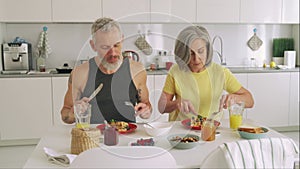 Happy healthy fit mature senior family couple having breakfast sit at kitchen.