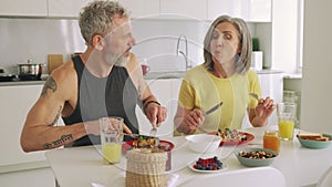 Happy healthy fit old family couple having breakfast sitting at kitchen table.