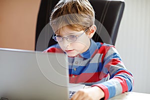 Happy healthy kid boy with glasses making school homework at home with notebook. Interested child writing essay with