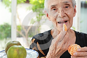 Happy healthy senior woman eating tangerine deliciously,asian old elderly opening her mouth wide to taste delicious organic orange