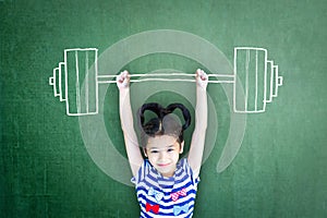 Happy healthy strong kid weight lifting on grunge green chalkboard background: International day of girl child Equality