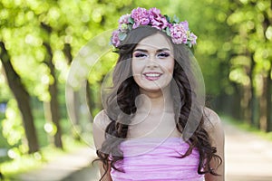Happy healthy woman with makeup and long wavy dark brown hairstyle with flowers on head in spring park outdoor
