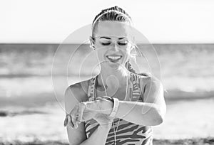 Happy healthy woman on seashore looking at activity tracker