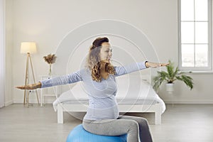 Happy healthy young woman doing gymnastic exercises with a yoga ball during pregnancy