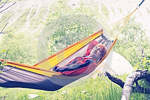 Happy hiker is relaxing in hammock on the alpine meadow