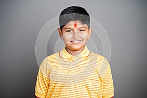 Happy Hindu kid with kumkum Bindi or Tilak on forehead by looking at camera on studio background - concept of smiling and positive