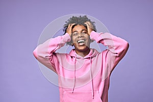 Happy hipster African American teen guy wearing pink hoodie isolated on purple.