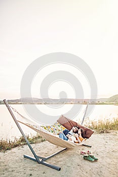 Happy hipster couple with bulldog relaxing in hammock on the beach in sunset light, summer vacation. stylish family with dog