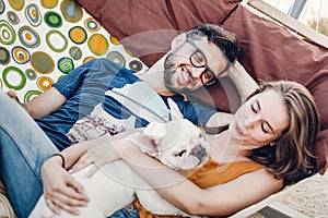 Happy hipster couple with bulldog relaxing in hammock on the beach in sunset light, summer vacation. stylish family with dog