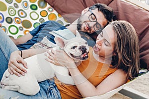 Happy hipster couple with bulldog relaxing in hammock on the beach in sunset light, summer vacation. stylish family with dog