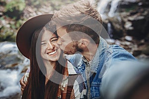 Happy hipster couple taking selfie at waterfall in forest. styli