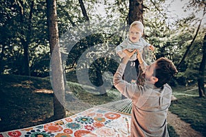 Happy hipster father playing with his cute little son on hammock in summer sunny park. stylish dad with kid relaxing in forest and