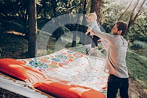 Happy hipster father playing with his cute little son on hammock in summer sunny park. stylish dad with kid relaxing in forest and