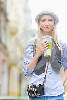 Happy hipster girl with cup of hot beverage on city street