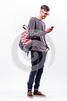 Happy hipster guy in glasses with backpack using a smart phone to listen music with headphones