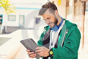 Happy hipster guy using his laptop while standing outdoors on a sunny day