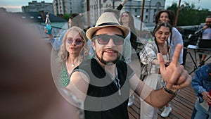 Happy hipster man blog vlog photo selfie at roof party discotheque dancing with friends crowd POV