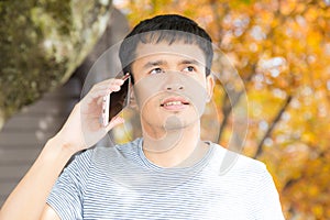 Happy hipster man walking in autumn park using mobile phone