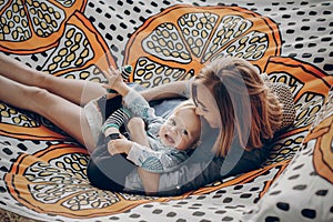 Happy hipster mother playing with her cute little son on hammock in summer sunny park. stylish mom with kid relaxing in forest and