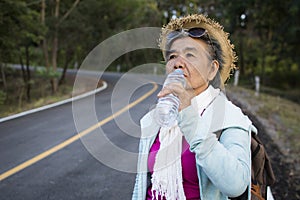 Happy hipster old women drinking water of bottle during backpack