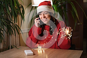 Happy hipster woman calling to friend and telling good news in Christmas eve.Emotional positive young woman in Santa hat