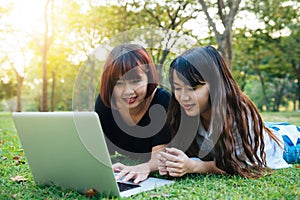 Happy hipster young asian women working on laptop in park. Student studying outdoors.