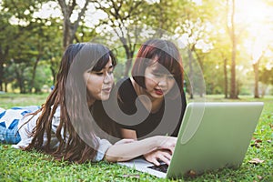 Happy hipster young asian women working on laptop in park. Student studying outdoors.