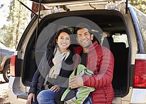 Happy Hispanic couple sitting in open back of car before hike