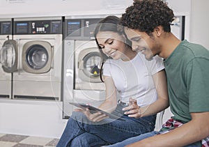 Happy Hispanic Couple Using Digital Tablet While Doing Laundry Indoor