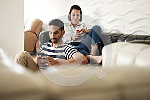 Happy Hispanic Couple Using Smartphones On Couch At Home