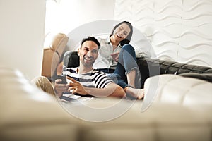 Happy Hispanic Couple Using Smartphones On Couch At Home