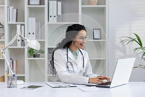 Happy Hispanic female doctor working at her office desk