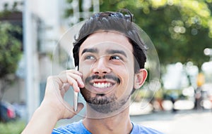 Happy hispanic guy at phone in city