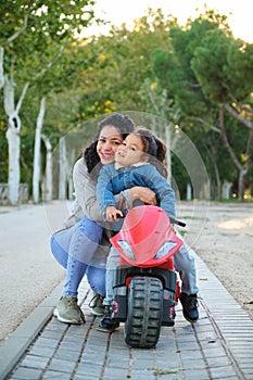 Happy Hispanic mother hugging her son on a balance bike in a park.