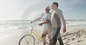 Happy hispanic senior couple walking with bikes on beach at sunset