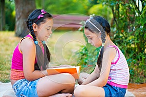 Happy hispanic sisters reading in the park